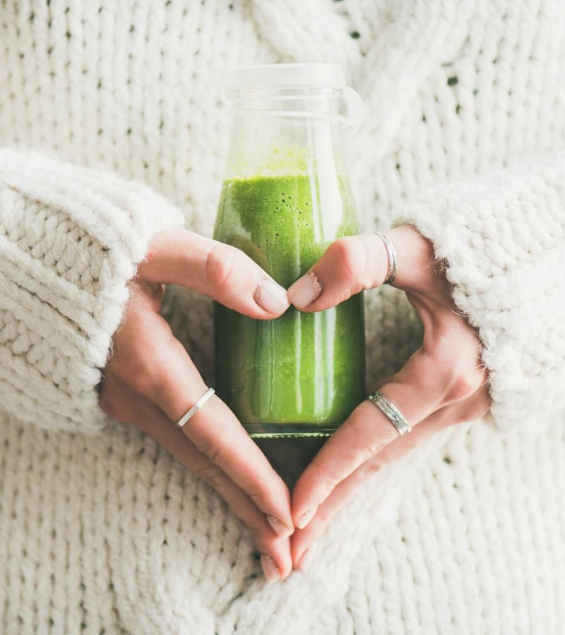 Winter seasonal smoothie drink detox. Female in woolen sweater holding bottle of green smoothie or juice making heart shape with her hands. Clean eating, weight loss, healthy dieting food concept